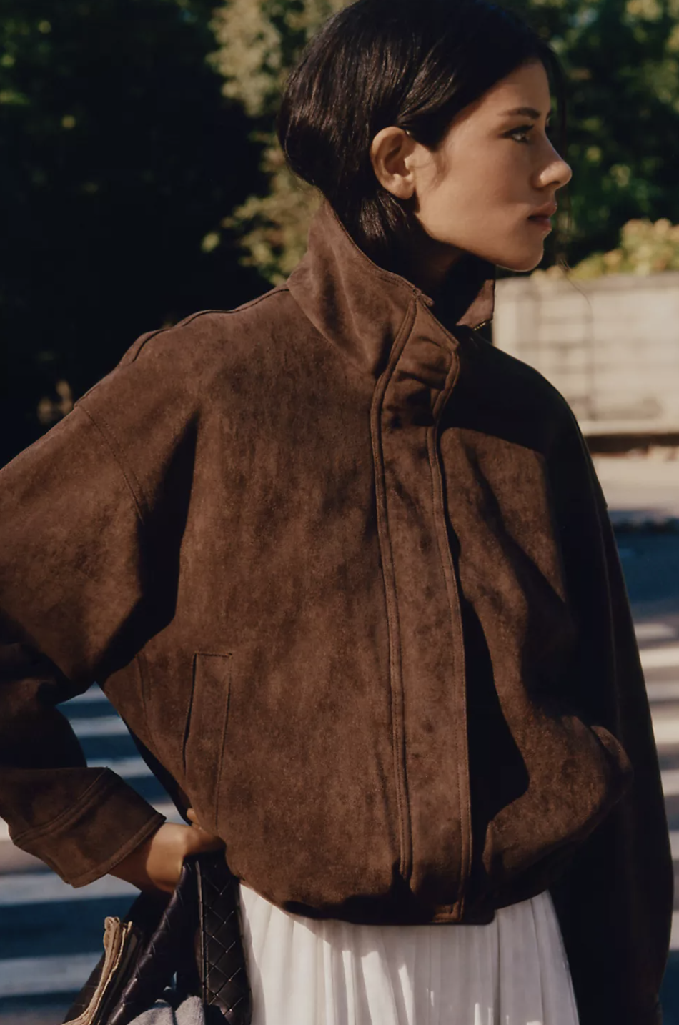 Woman wearing the Maeve Imara brown faux-suede funnel-neck jacket paired with a white skirt set against an outdoor backdrop.