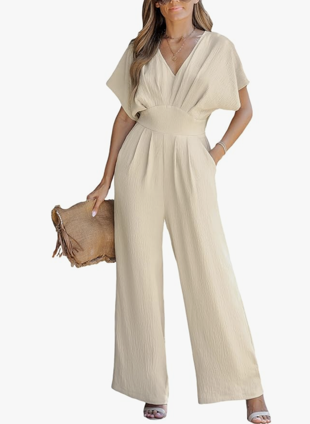 A woman wearing a beige v-neck short sleeve jumpsuit with a waist tie, styled as a polished and comfortable dinner outfit for a cruise.