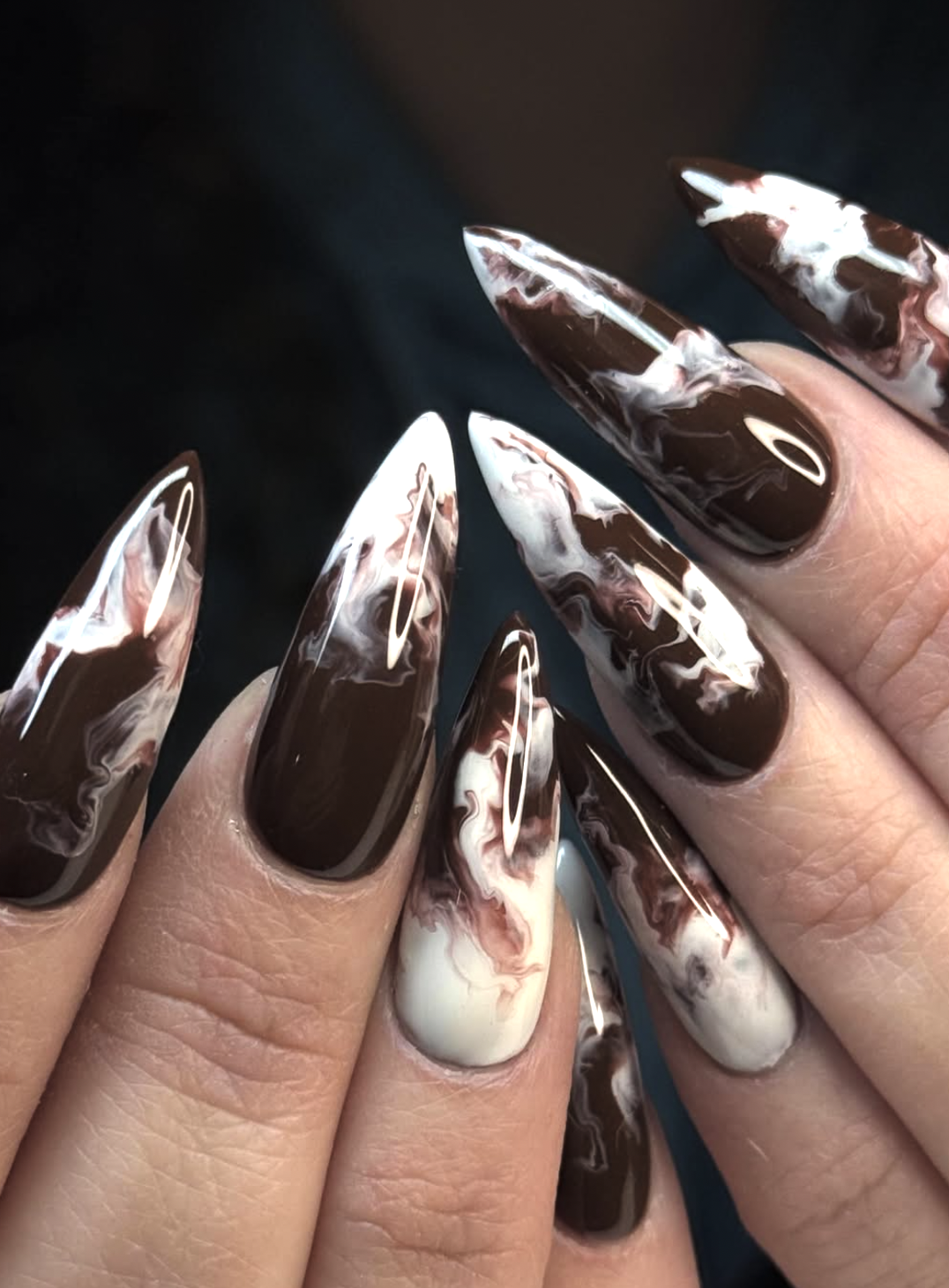 Abstract chocolate brown and cream swirls over a sheer nude nail base.