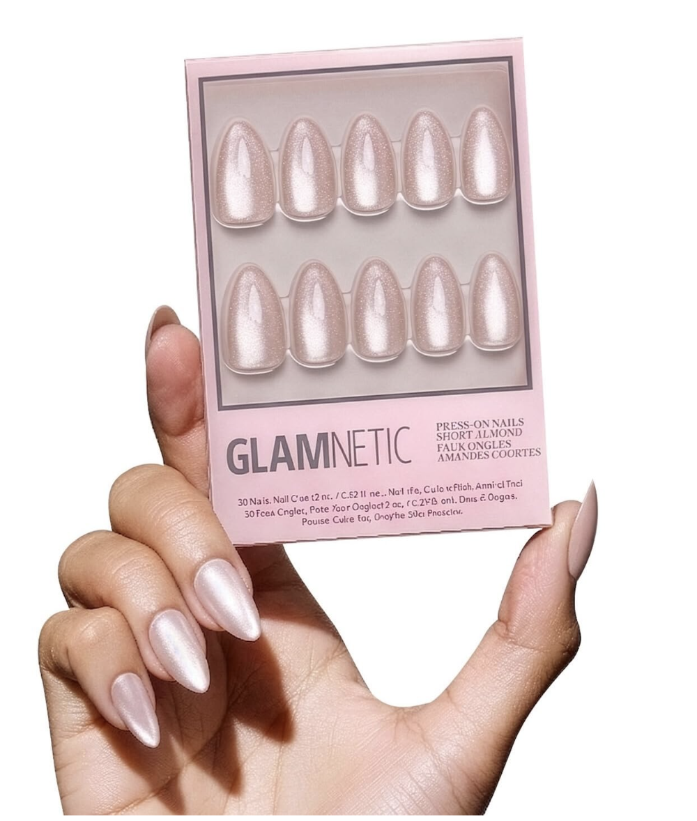 Hand wearing Glamnetic The Vow shimmery pale pink short almond press-on nails while holding the package.