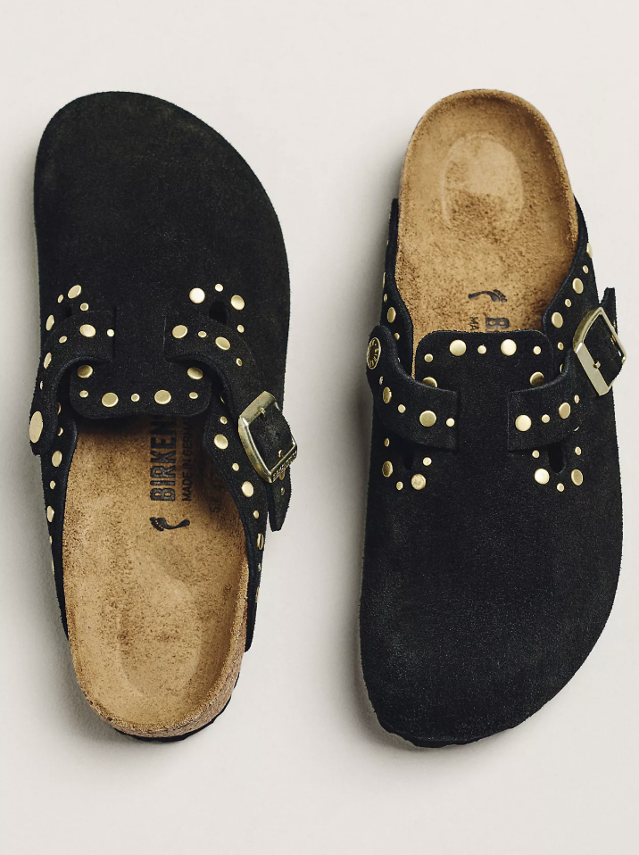 A close-up view of a pair of black suede Birkenstock Boston clogs featuring a gold buckle strap and intricate gold stud detailing along the upper.