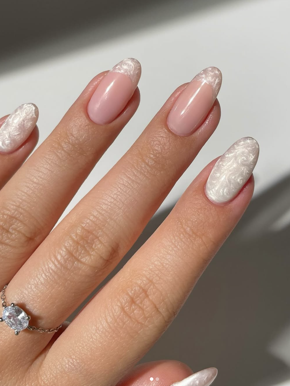 Long almond-shaped nails with a sheer pink base and white French tips featuring an intricate, embossed lace and floral texture with a soft pearl finish.
