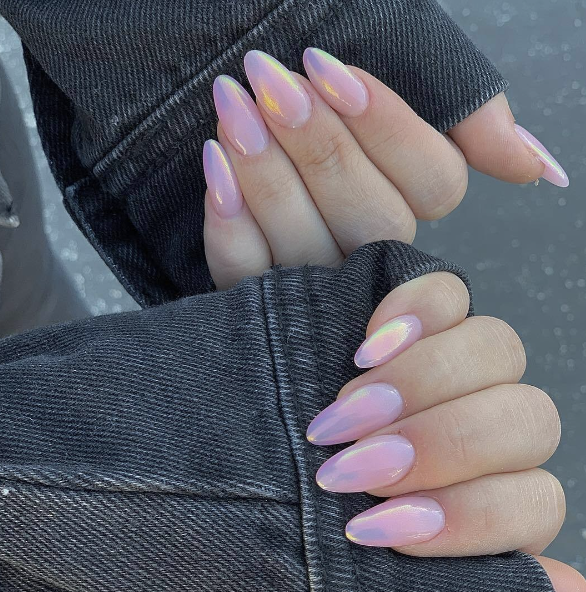 A close-up of almond-shaped nails with a soft cotton candy pink base and a shimmering iridescent finish.