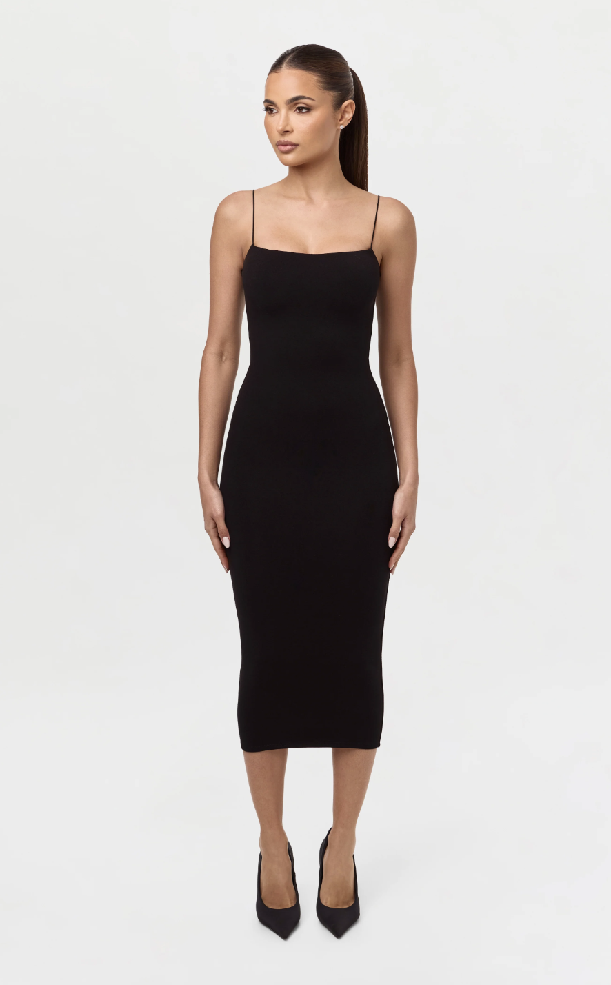 A woman wearing a sleeveless black bodycon midi dress with pointed-toe pumps, representing a versatile spring 2026 wardrobe staple.