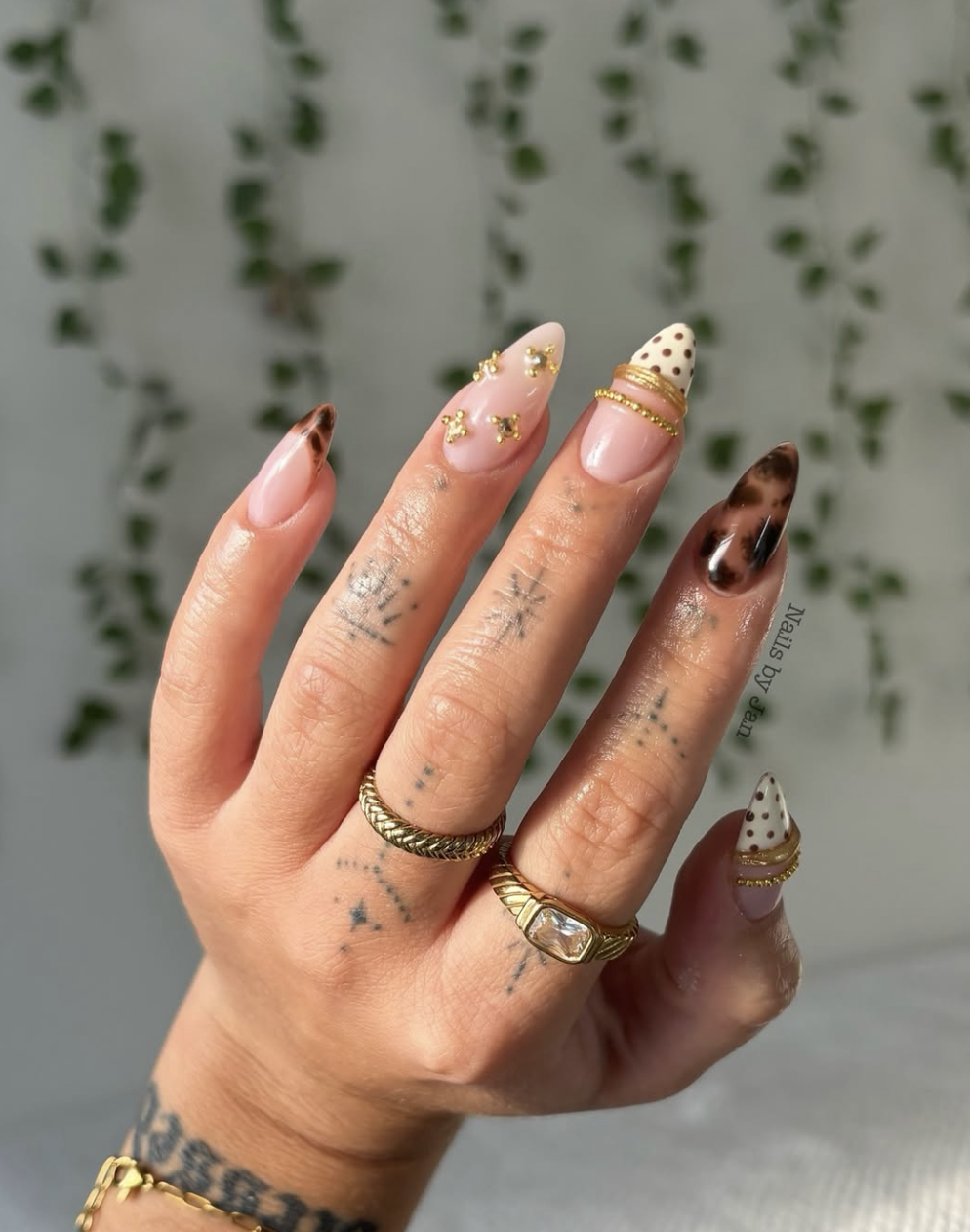Close-up of almond-shaped nails featuring a mix of tortoise print, white polka dots, and 3D gold bangle accents with star charms.