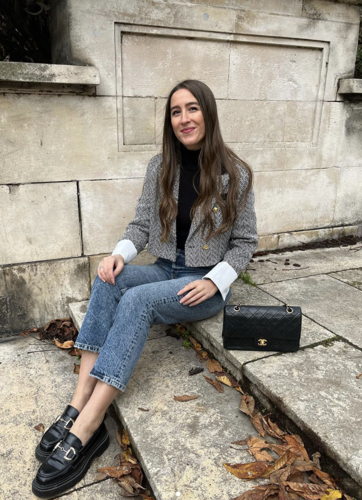 A woman wearing a grey patterned cropped blazer over a black turtleneck and blue jeans, styled with black leather Mary Jane flats for women.