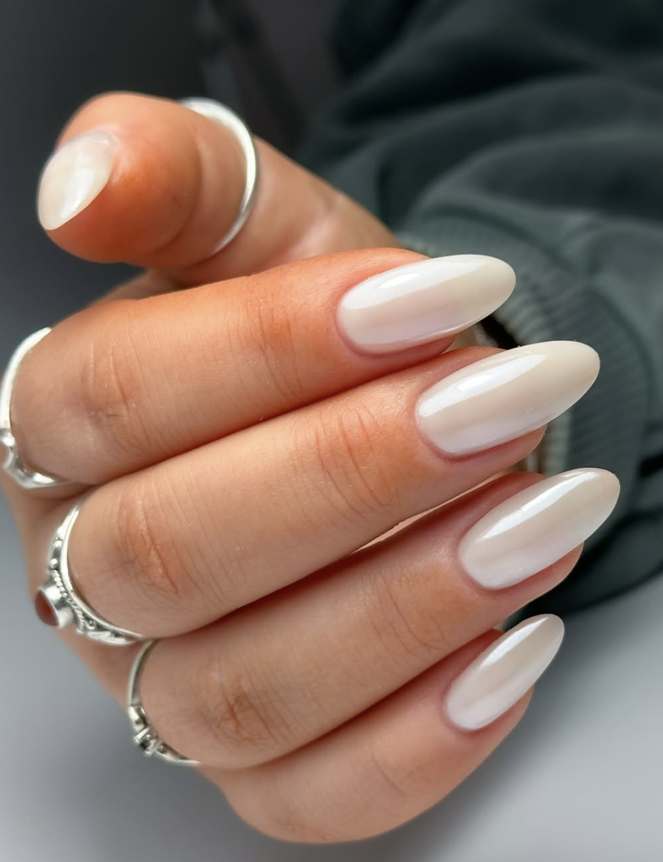 A close-up of a hand with short, rounded nails showcasing a classic pearl glazed donut finish with a luminous chrome shimmer.