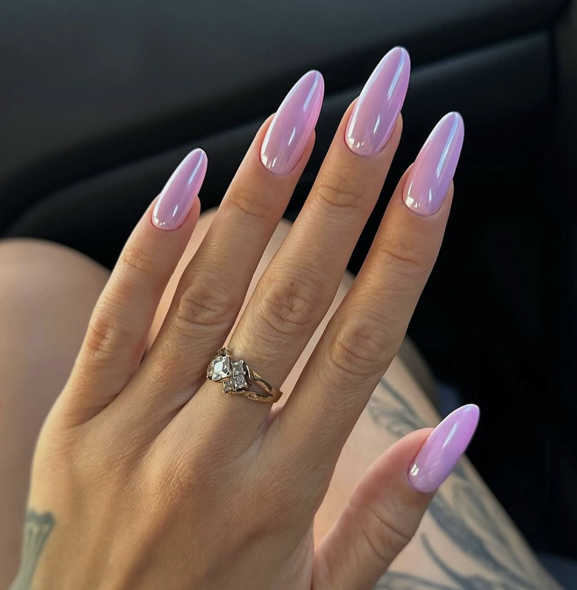 A close-up of long, oval-shaped nails with a cool-toned lilac-pink chrome finish and a high-shine metallic reflection.