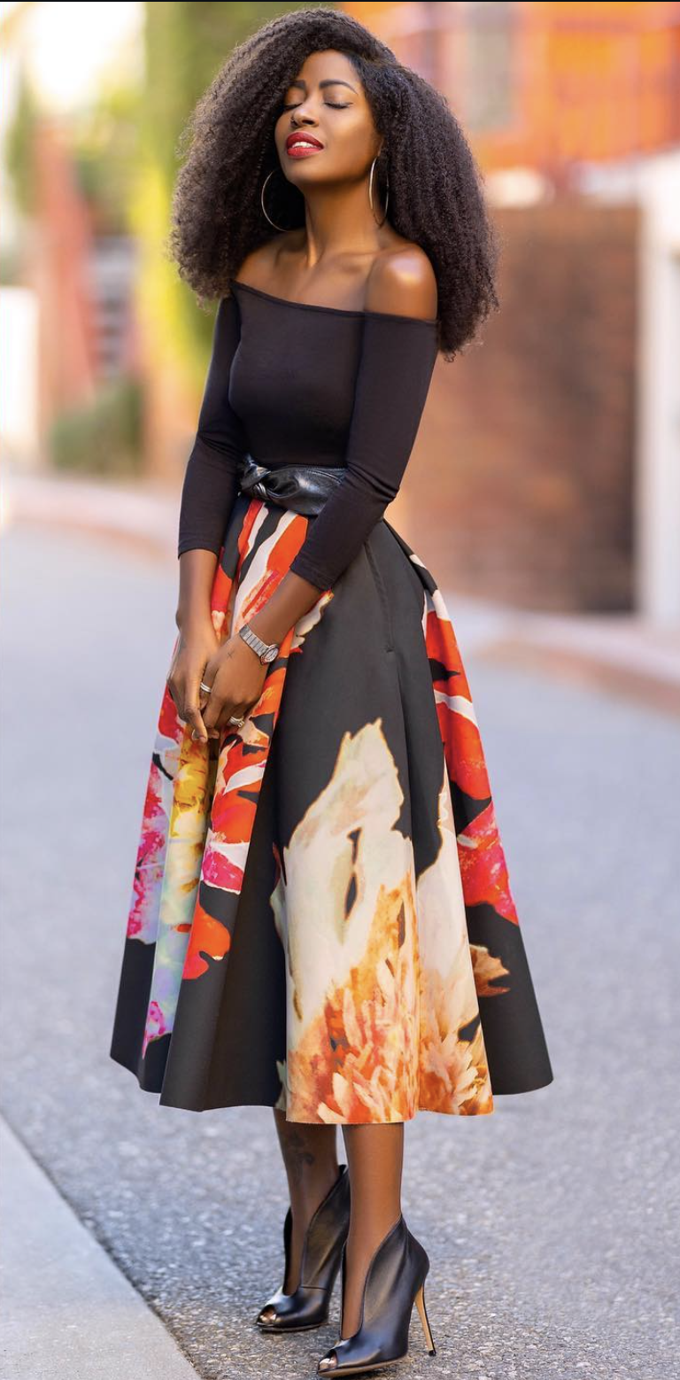Woman wearing a full floral midi skirt with a black off-the-shoulder top, wide belt and pointed stiletto booties