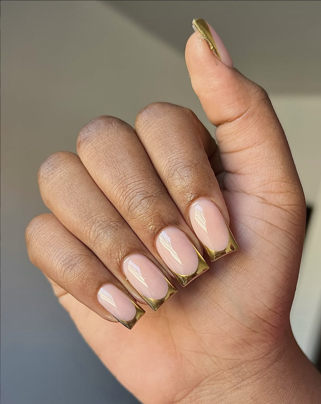 Close-up of short squoval nails featuring a metallic gold chrome micro French tip over a glossy sheer nude base.