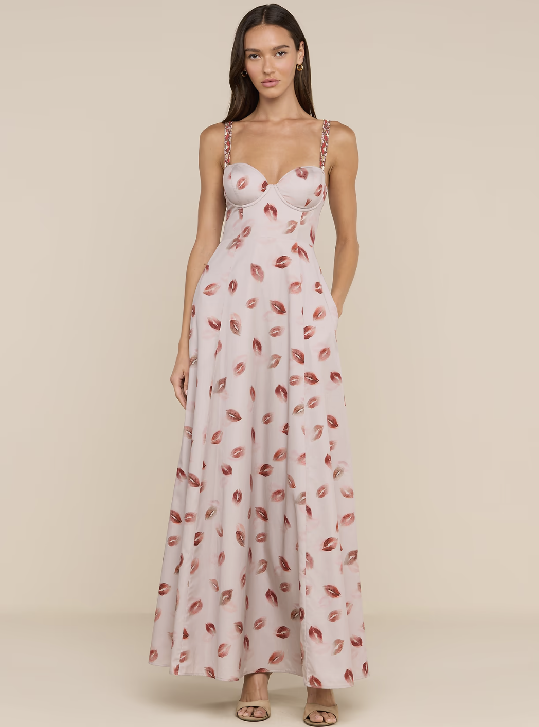 A woman wearing a light pink sleeveless maxi dress featuring a sweetheart neckline and an all-over red lip print.
