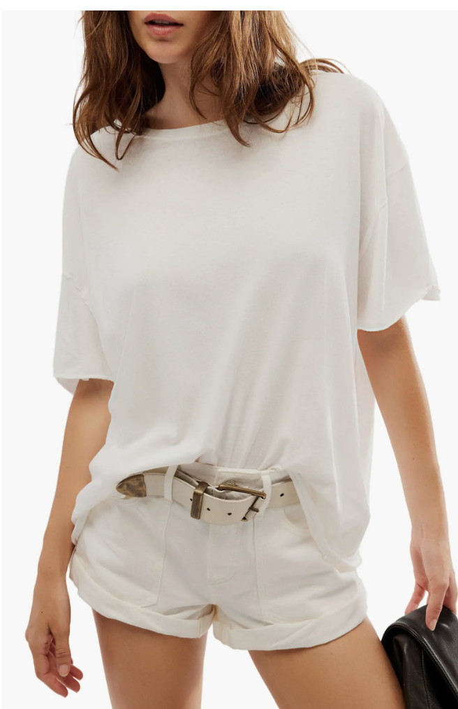 A person wearing an oversized white crew neck t-shirt with drop shoulders and a raw-edge hem, styled with white cargo shorts and a tan leather belt.