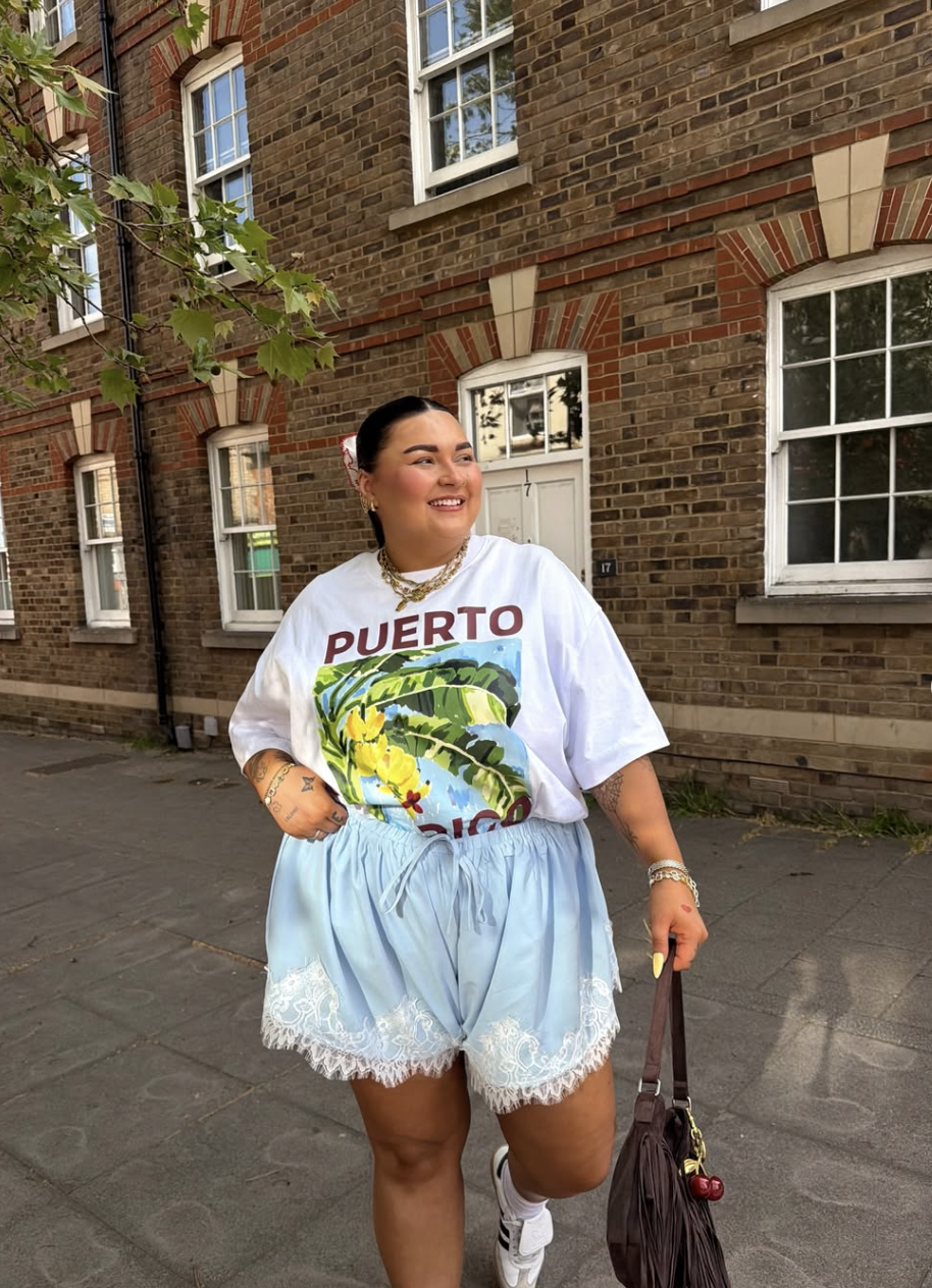 Plus-size woman wearing an oversized white graphic t-shirt that says "Puerto Rico" paired with light blue lace-trimmed shorts.