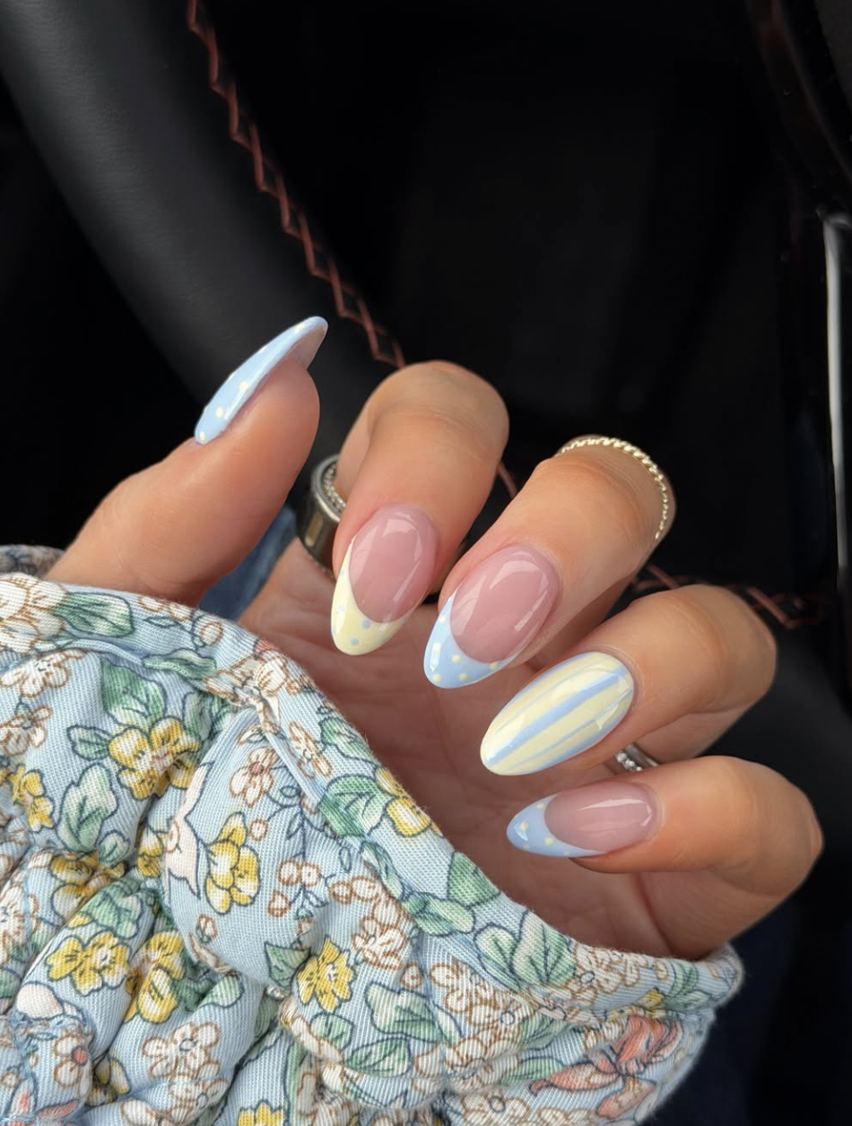 High feminine spring nail art by @fashionablykay featuring elegant almond-shaped nails with baby blue and butter yellow patterns, soft stripes, and delicate polka dots.