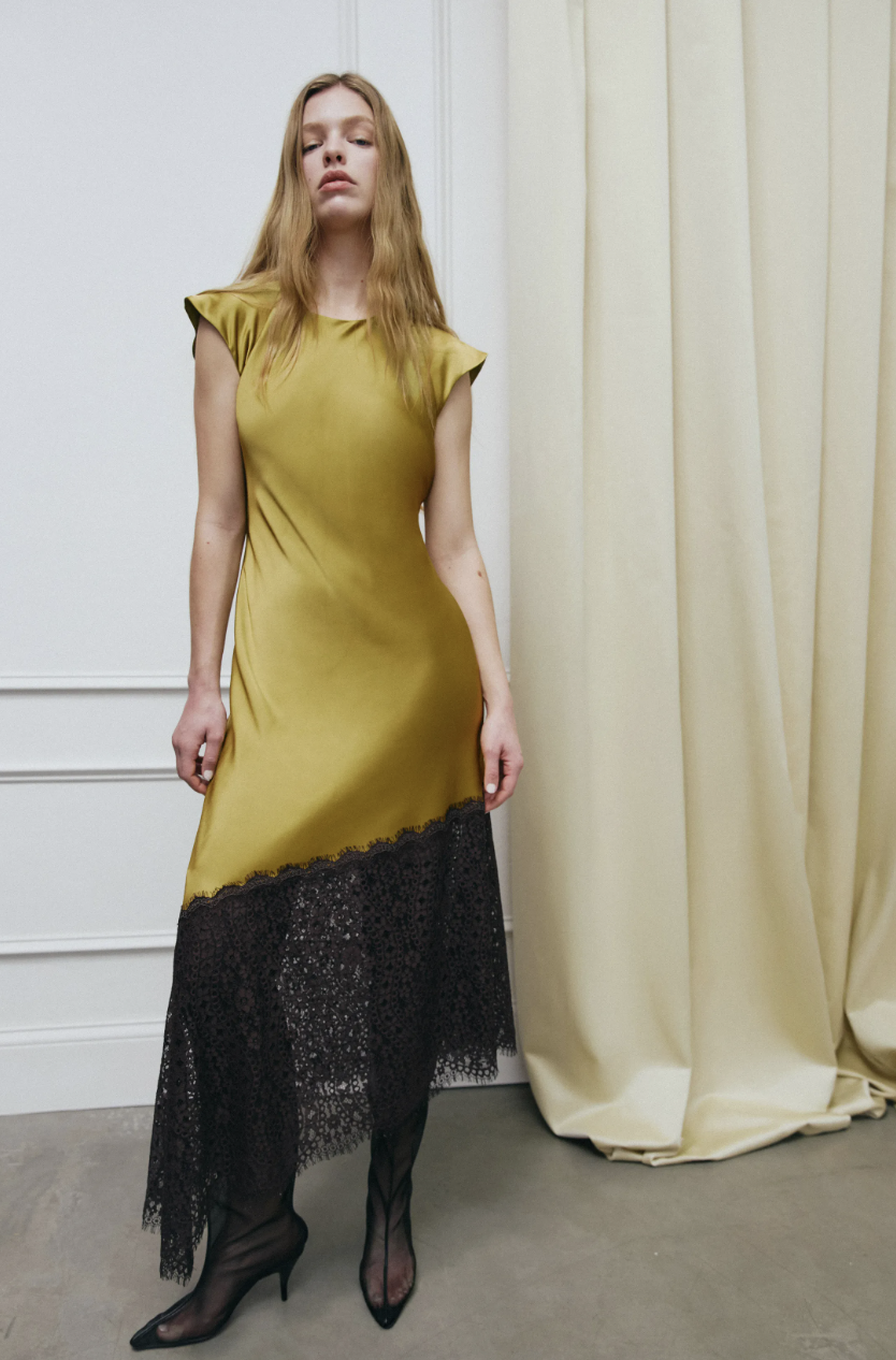 A model on the Tanya Taylor Fall/Winter 2026 runway wearing a butter yellow top paired with a black lace midi skirt, showcasing the season's grown-up yellow color trend.