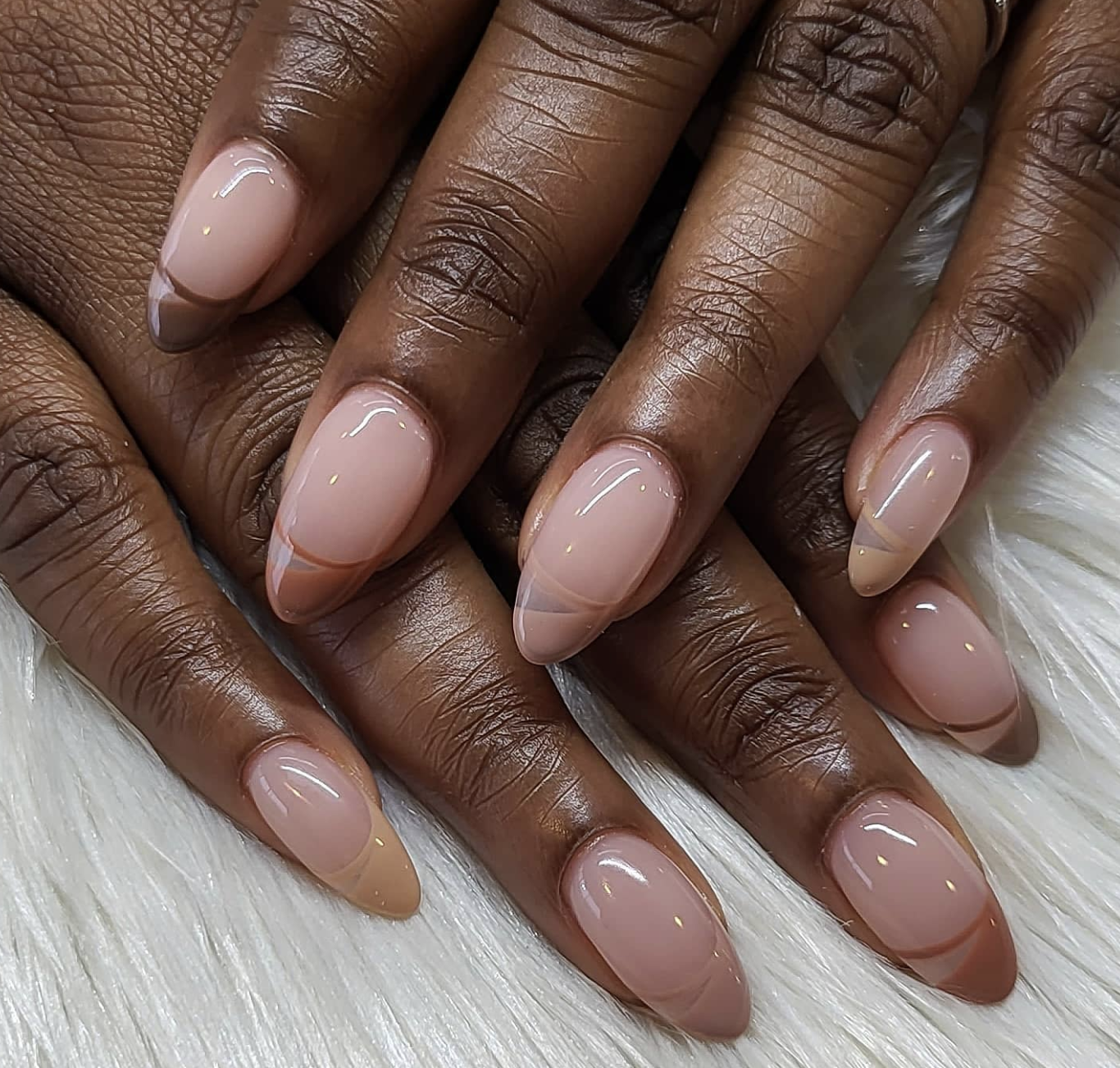A close-up of almond-shaped nails featuring smooth caramel brown French tips over a sheer peachy nude base.