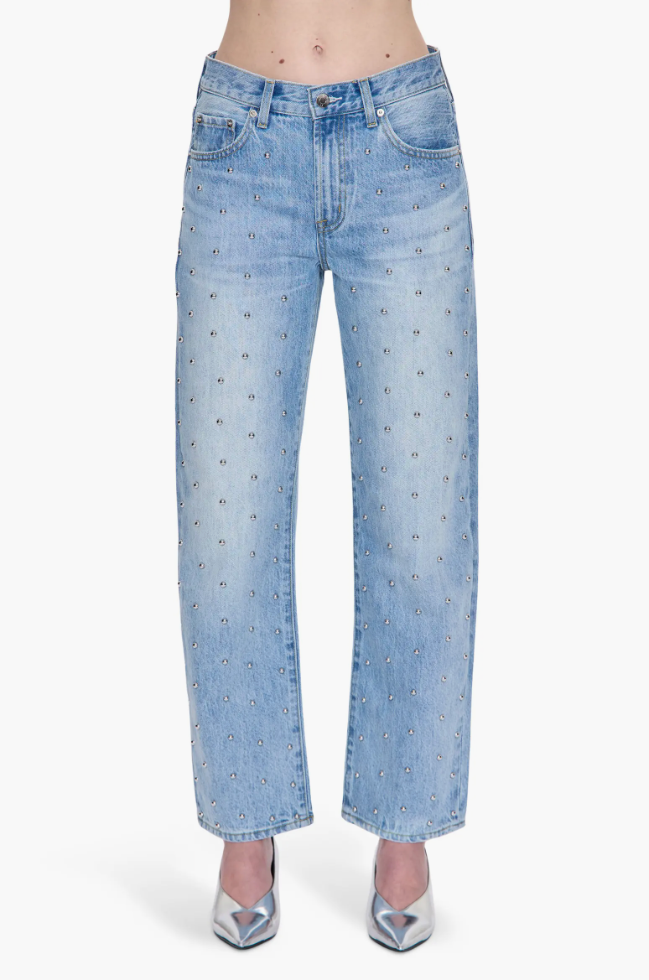 A close-up of light-wash, high-waisted barrel jeans embellished with small, silver stud details throughout the denim.