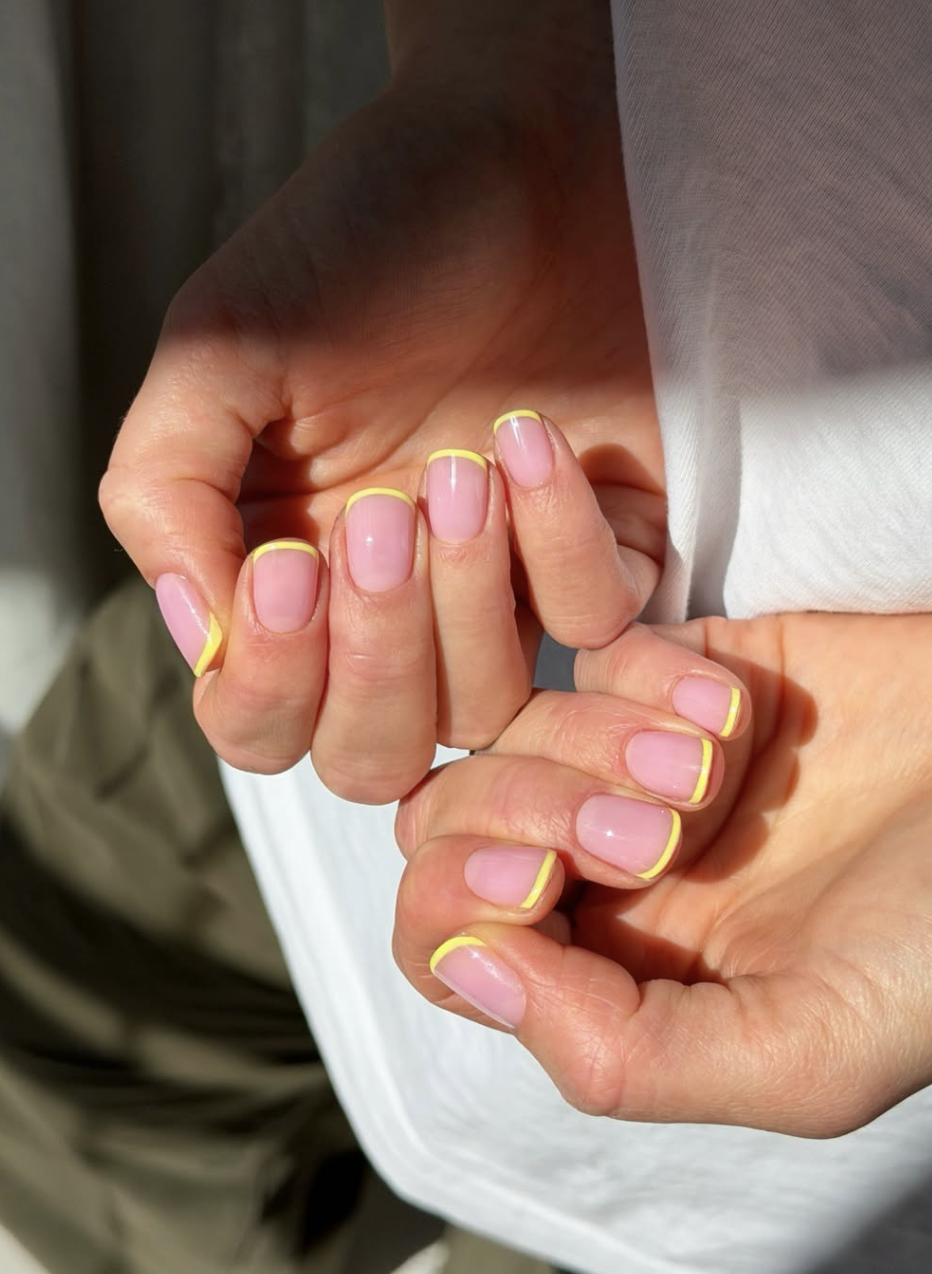 Close-up of short rounded nails featuring a bright neon yellow micro French tip over a glossy sheer pink base.