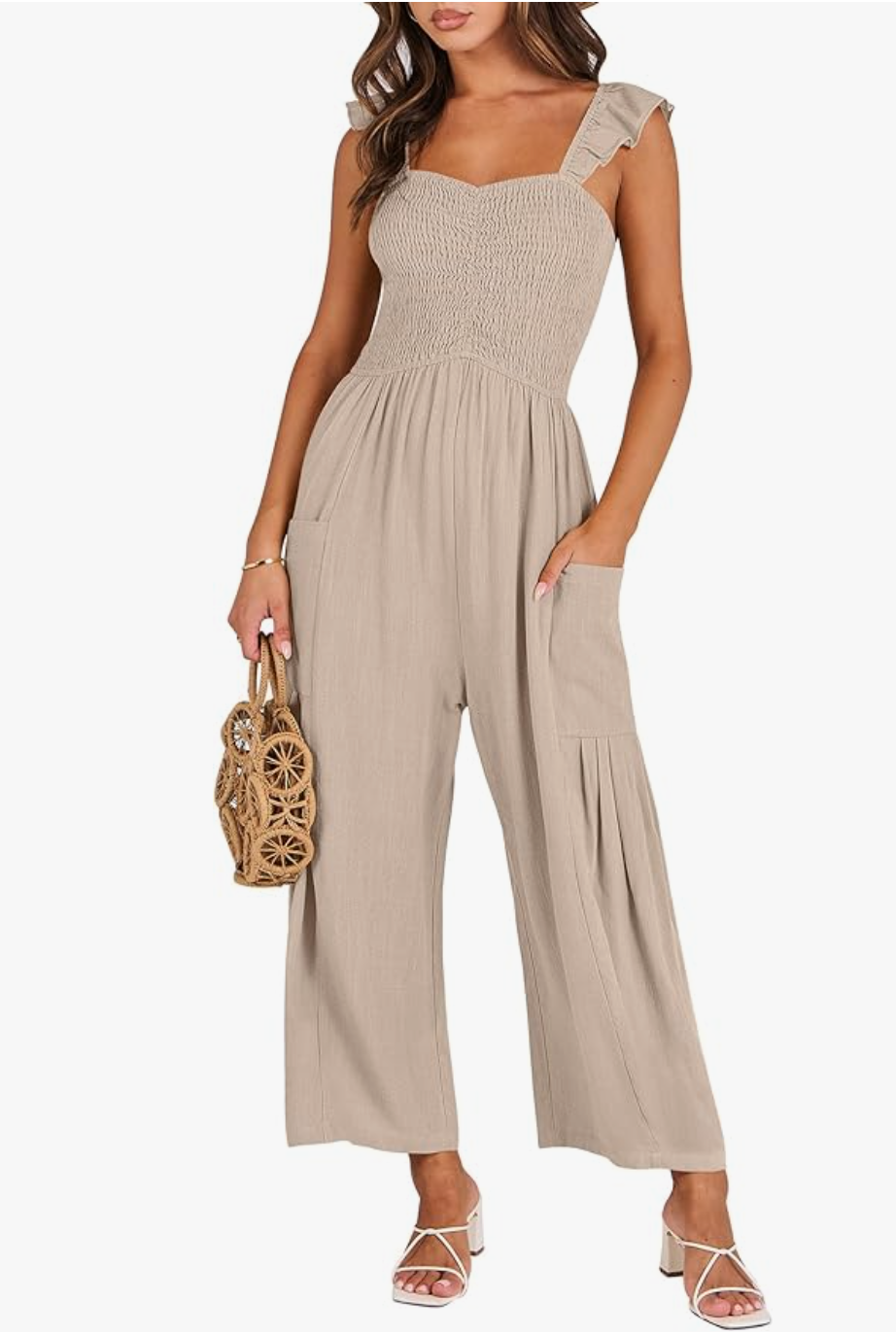 A woman wearing a khaki-colored sleeveless jumpsuit with a smocked bodice, wide-leg trousers, and functional side pockets.