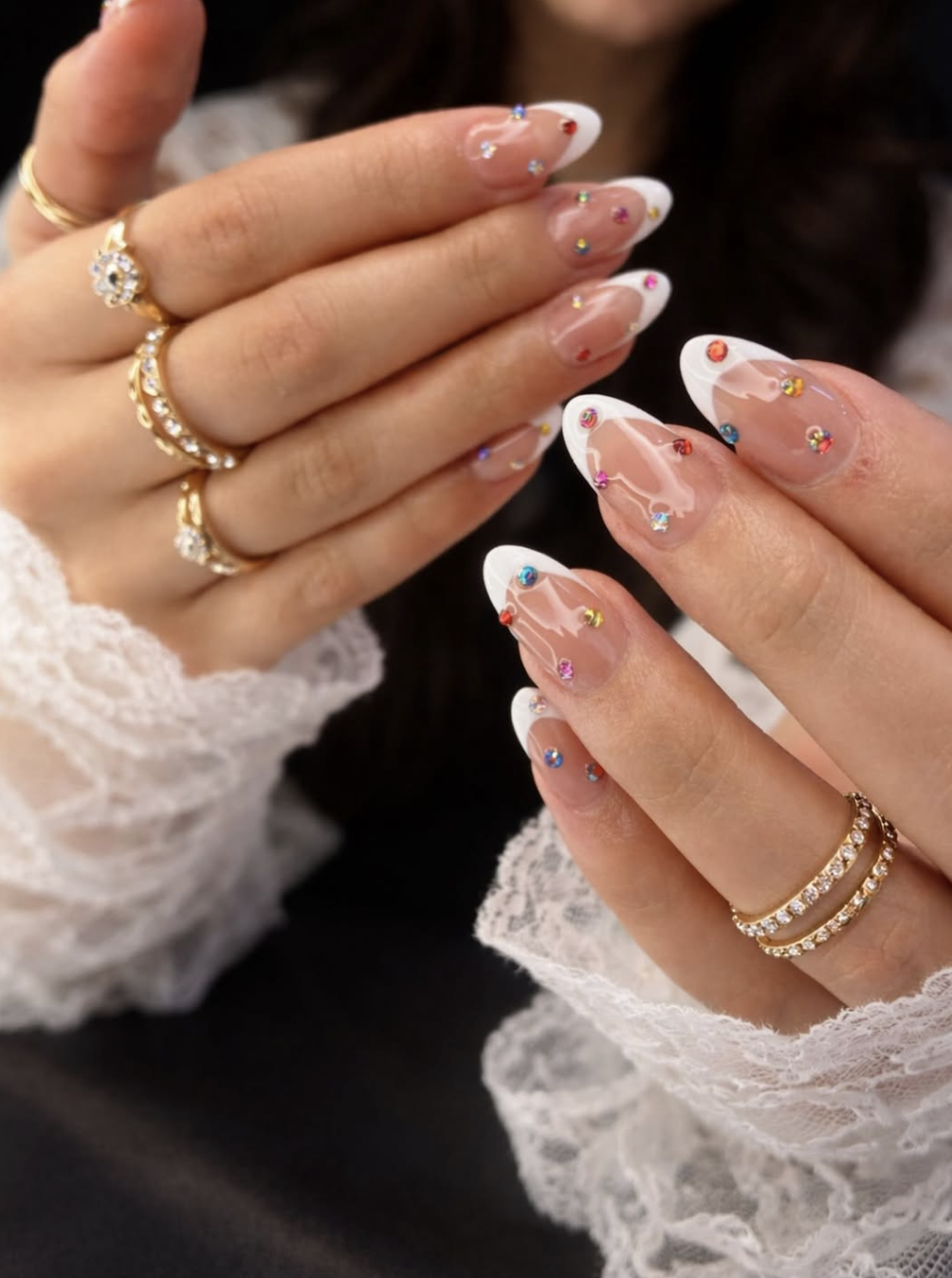 Long almond-shaped nails with a classic white French tip and multi-colored rhinestones precisely placed along the curved smile line.