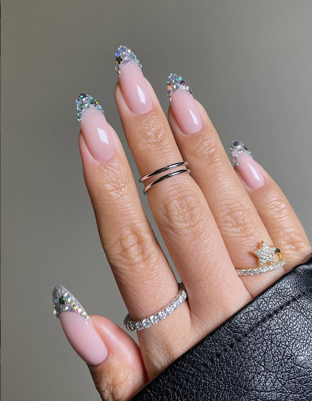 Long, almond-shaped nails featuring a translucent nude base with a dramatic silver glitter French tip fade.