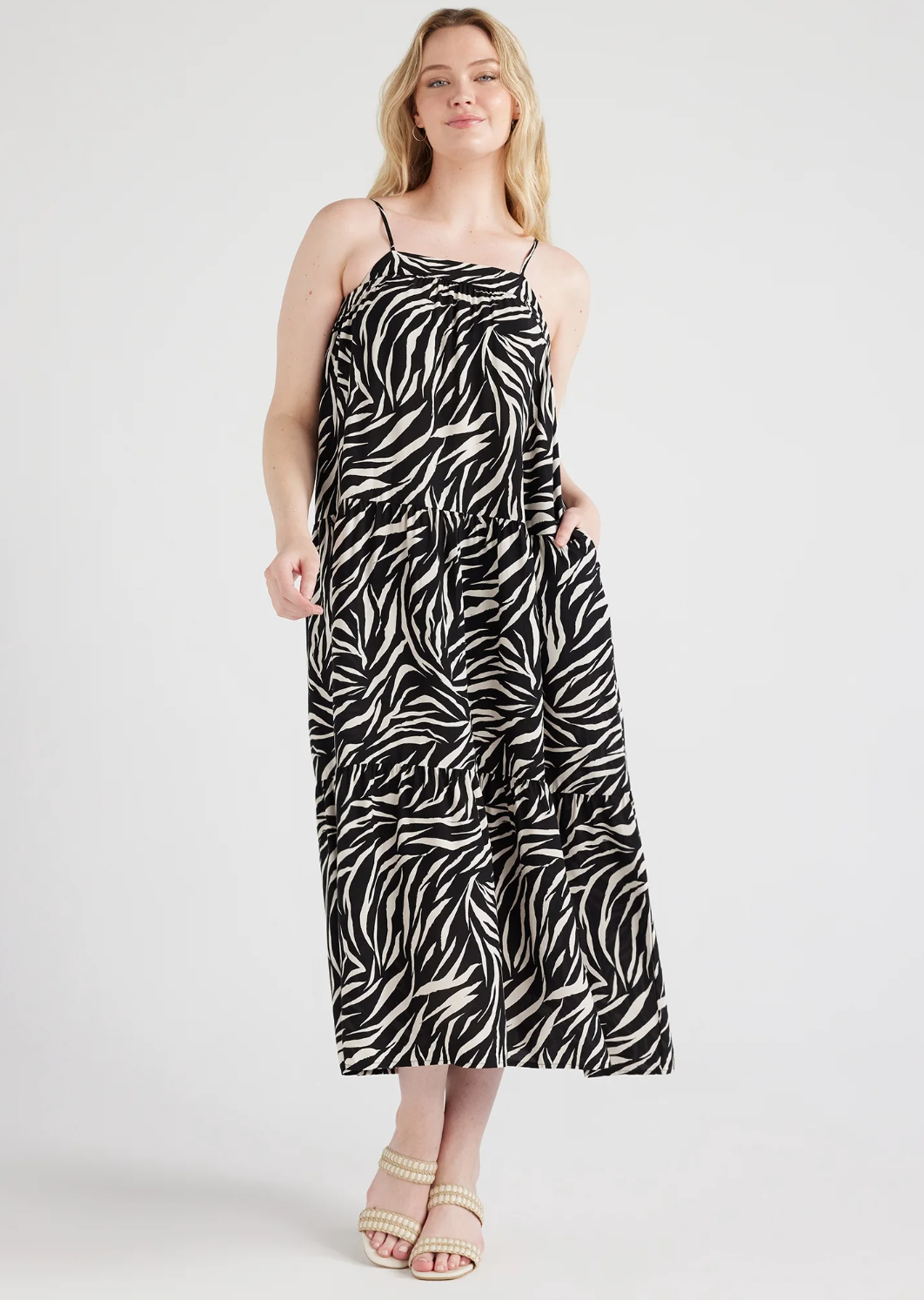 A person with an hourglass figure wearing a black and white zebra-print sleeveless smocked midi dress from Walmart, styled with neutral braided heeled sandals to showcase the flowy silhouette and flattering empire waist.