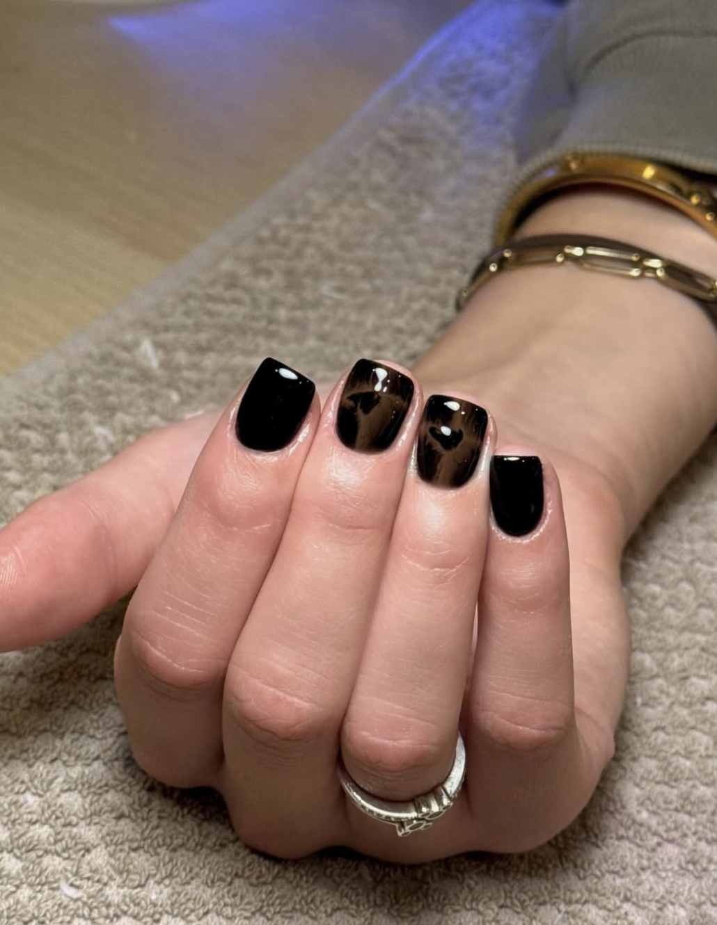 A hand with short, squoval nails featuring a glossy black nail polish manicure accented with rings.