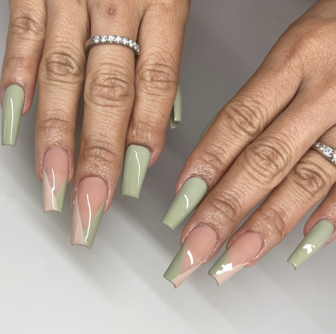 A close-up of long, square nails featuring a vertical half-and-half design with solid mint green and a sheer nude base.