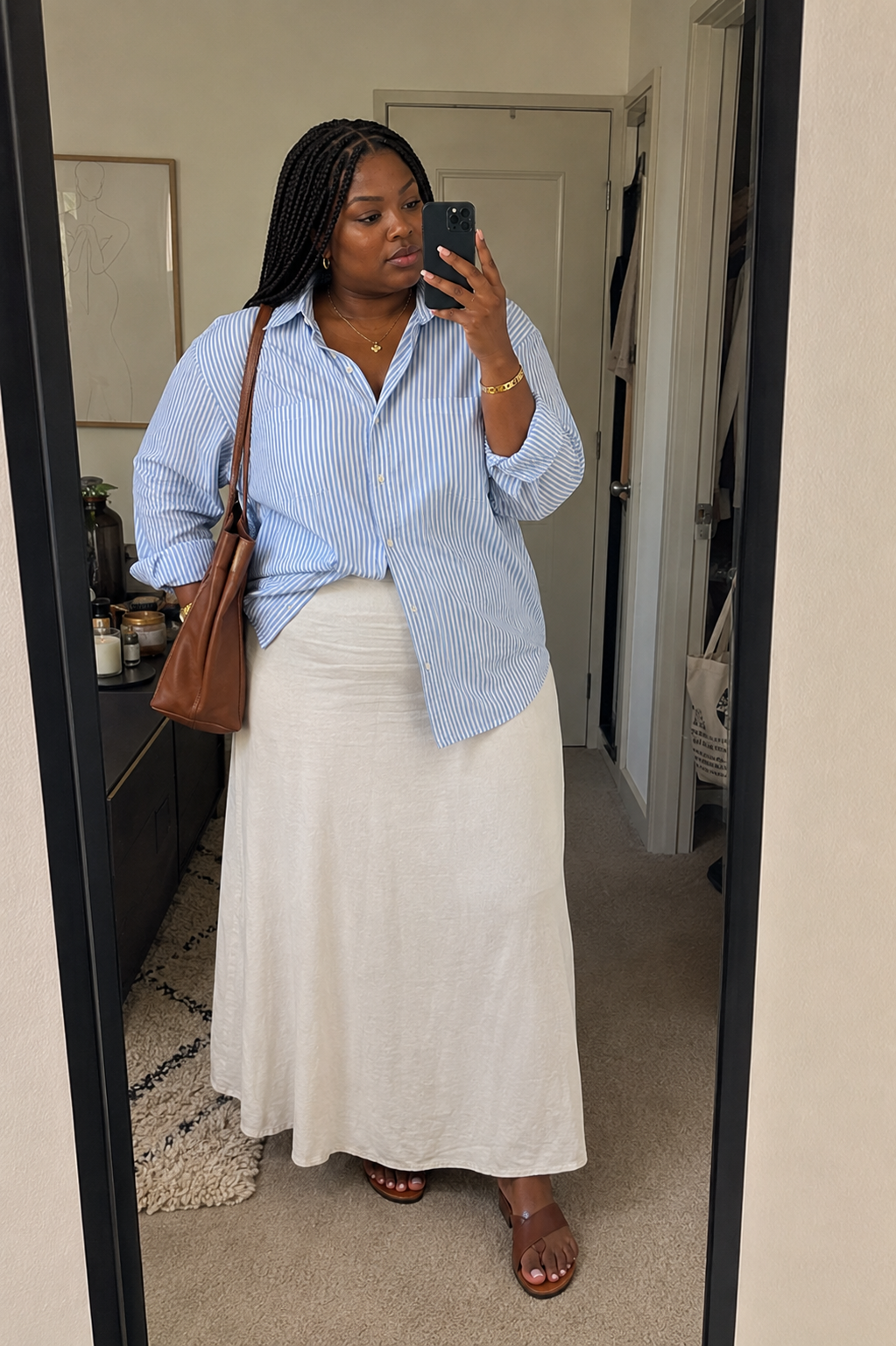 Close-up of a cream linen maxi skirt paired with a blue and white striped button-down shirt and a brown leather shoulder bag.