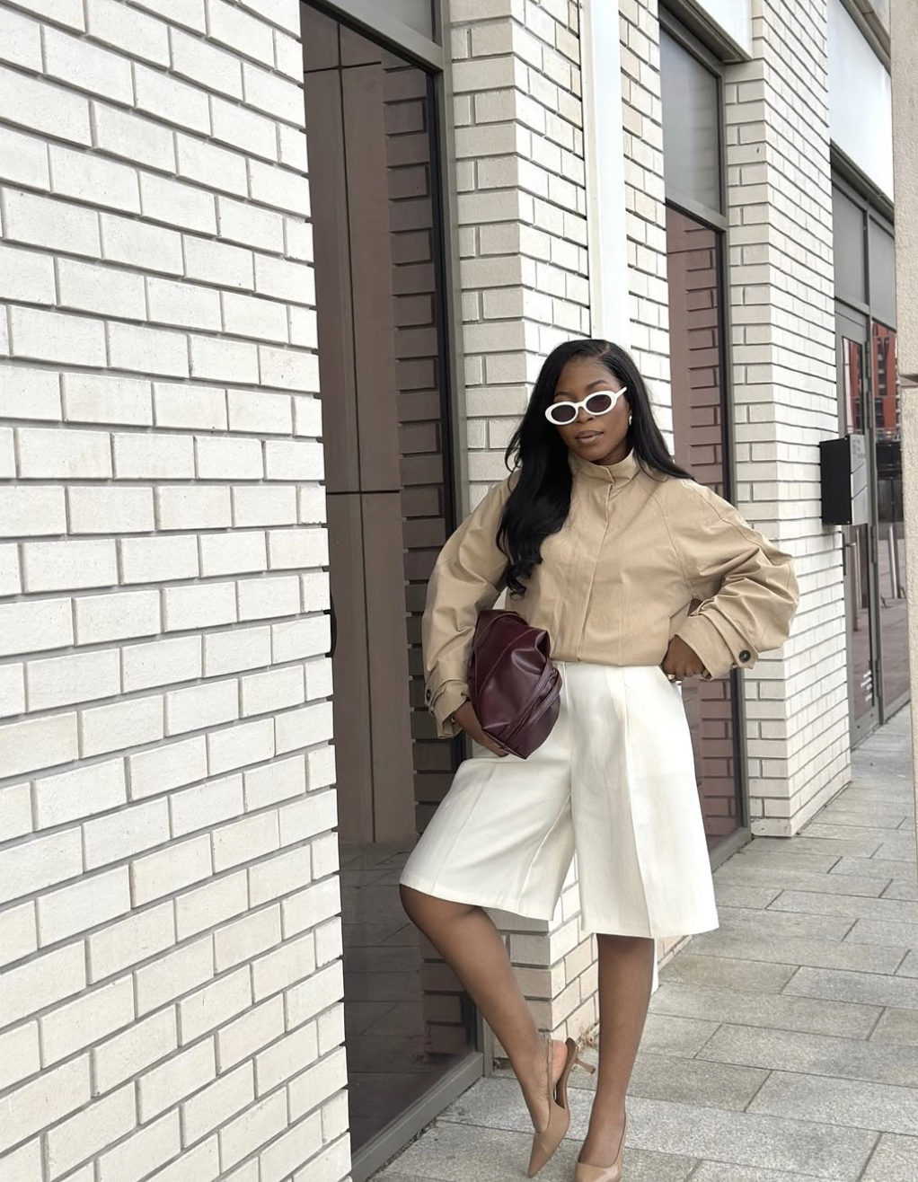 Camel high-neck top paired with white Bermuda shorts, nude pumps, and a burgundy clutch.