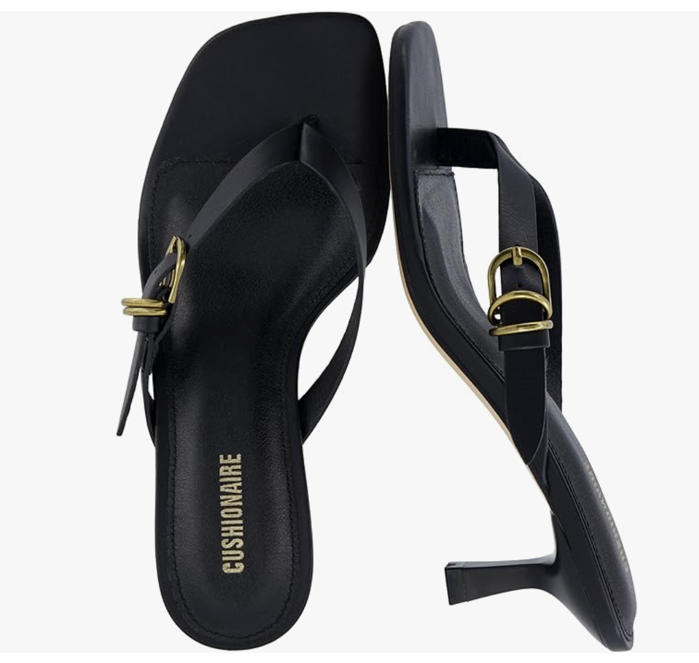 A pair of black Cushionaire brand strappy flip-flop sandals with a gold buckle detail on the outer strap and a low block heel.