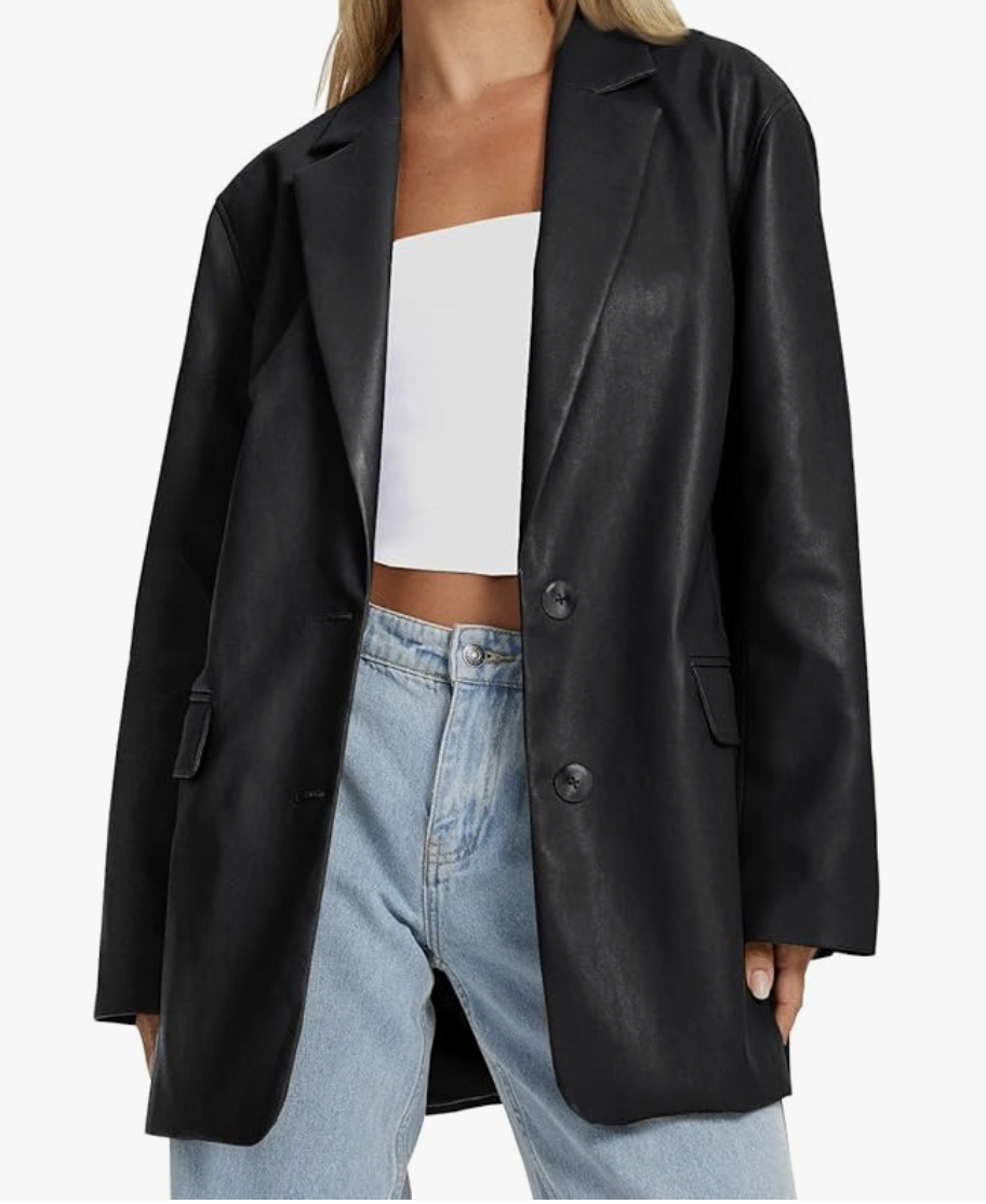 A close-up of a woman wearing a structured black faux leather blazer over a white top and light wash denim jeans.