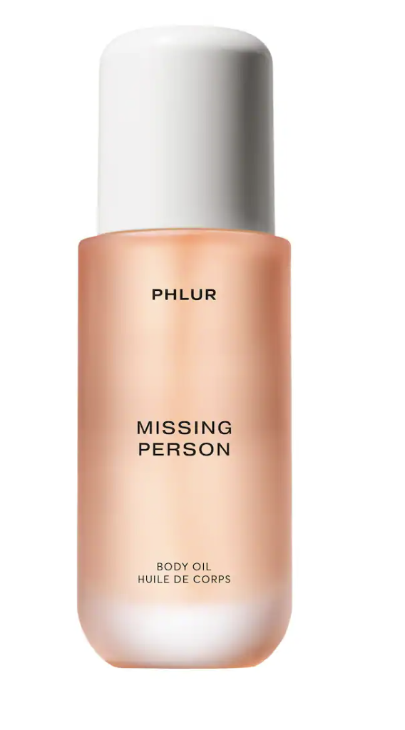 A sleek, frosted glass bottle of PHLUR Missing Person Body Oil with a white pump, containing a light peach-colored oil on a transparent background.