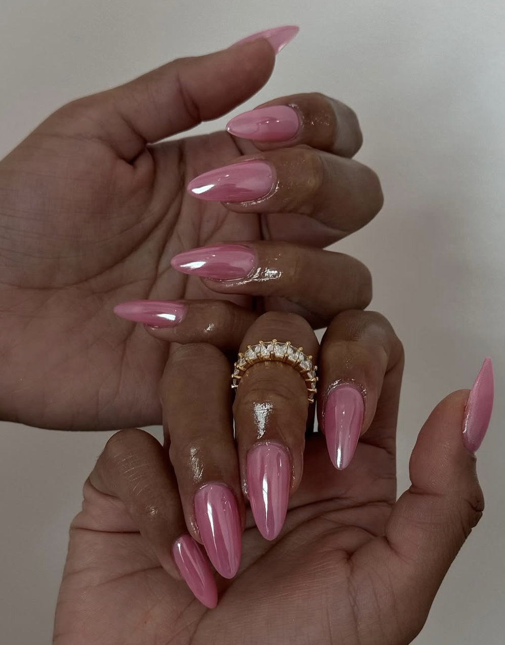 A close-up of long, tapered nails with a high-shine light pink chrome finish and iridescent metallic reflection.
