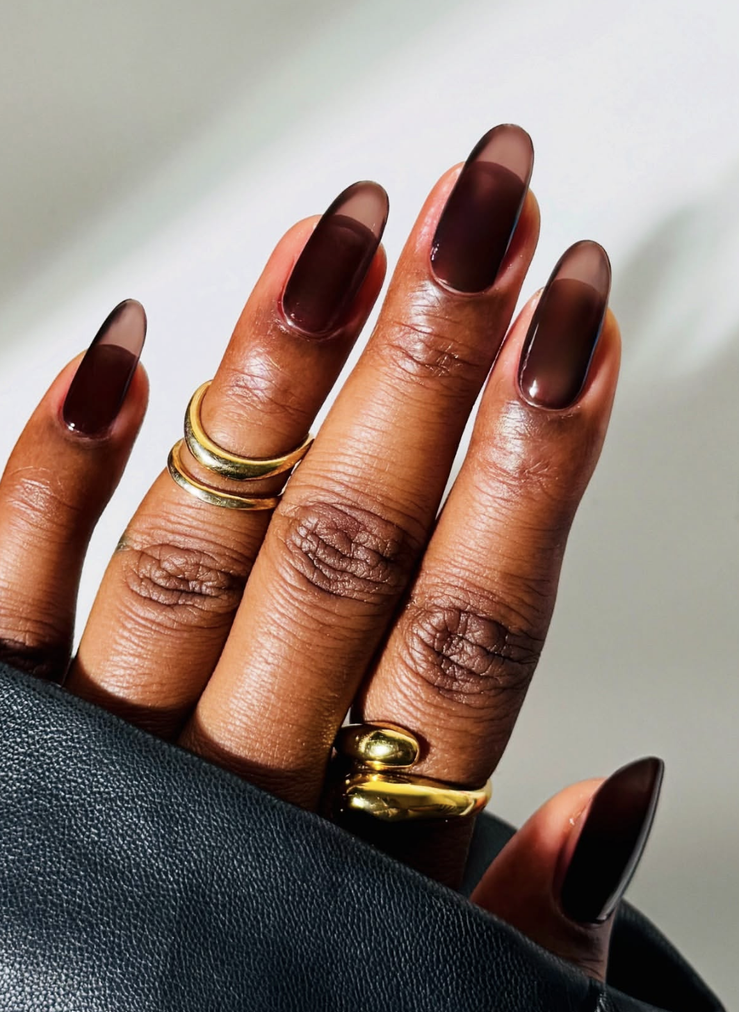 Long almond-shaped gel nails in a sheer, translucent dark brown jelly finish.