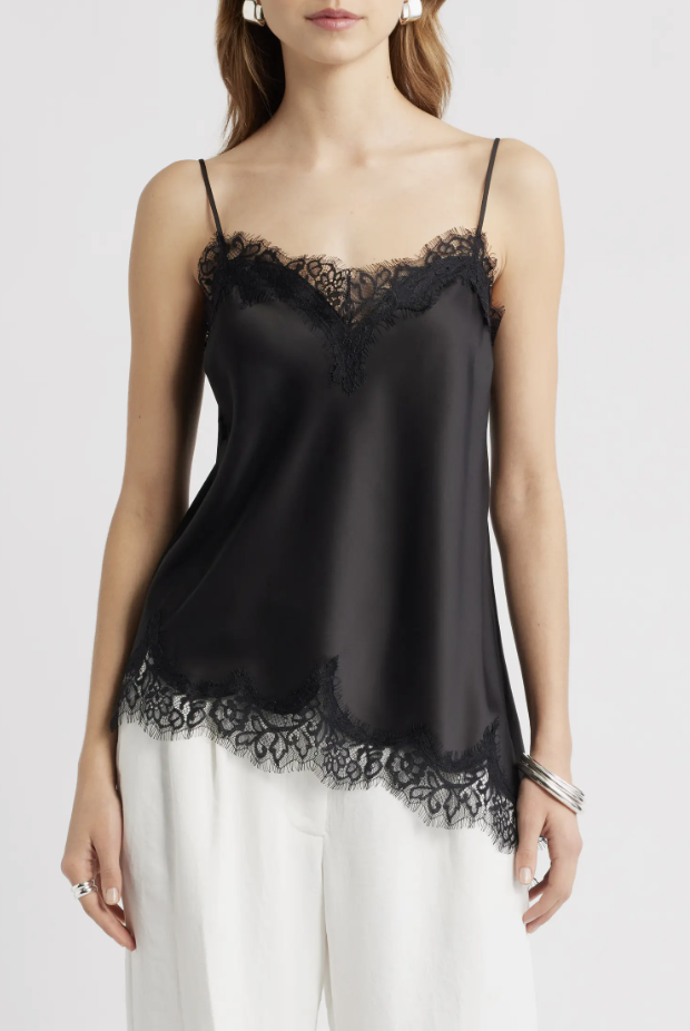 Close-up of a woman wearing a black satin camisole with delicate lace trim along the V-neckline, styled with white high-waisted trousers.