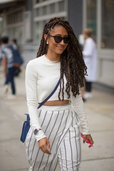 Elaine Welteroth wearing long, sleek Senegalese twists with a side part, styled with black sunglasses and a white long-sleeve crop top.