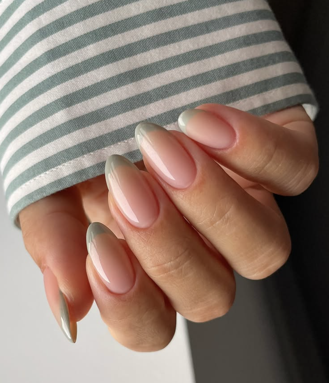 Medium almond-shaped nails featuring a glossy nude base with shimmering metallic sage green chrome French tips.