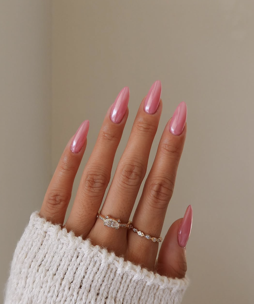 A close-up of almond-shaped nails with a soft blush pink base and a shimmering, pearlescent chrome finish.