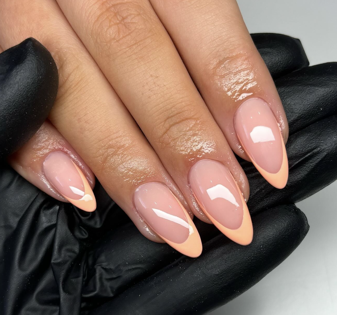 Long almond-shaped nails with a peachy-nude base, light peach French tips, and delicate gold foil accents.
