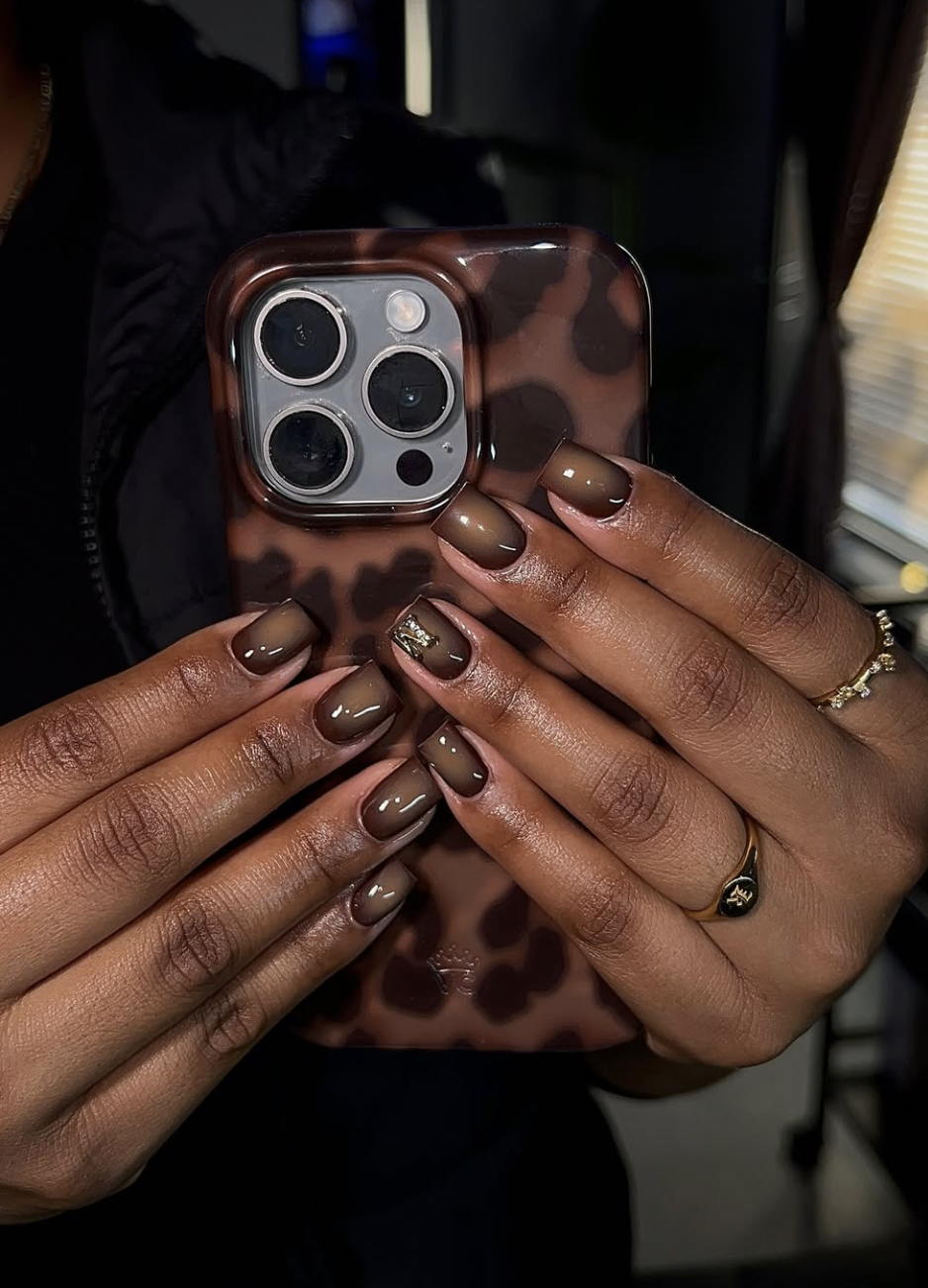 A close-up of hands with a glossy dark espresso brown manicure holding a phone with a leopard print case.