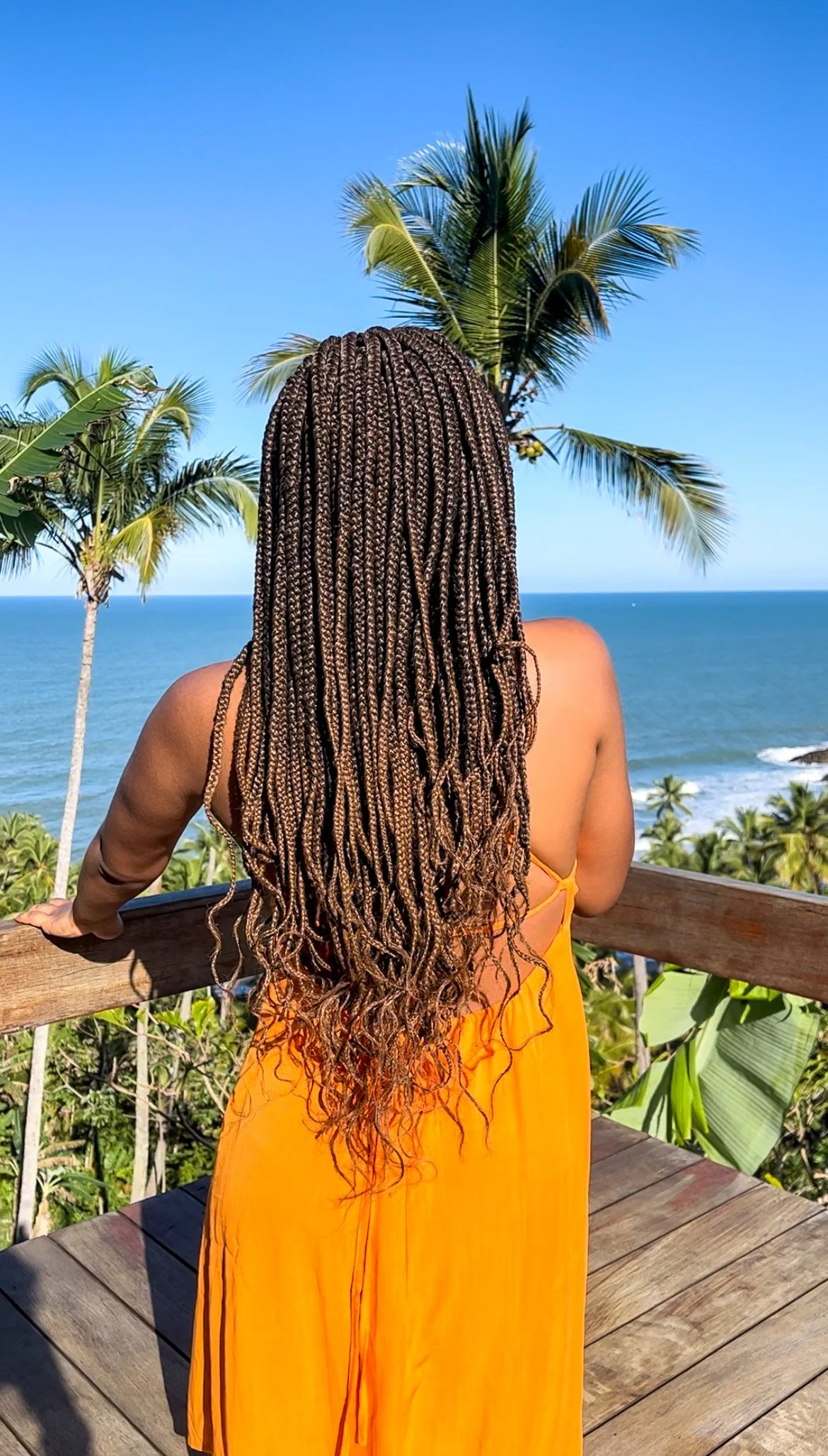Woman wearing a spaghetti strap dress with box braids overlooking the ocean, illustrating what to wear with a spaghetti strap dress for a summer or vacation outfit.