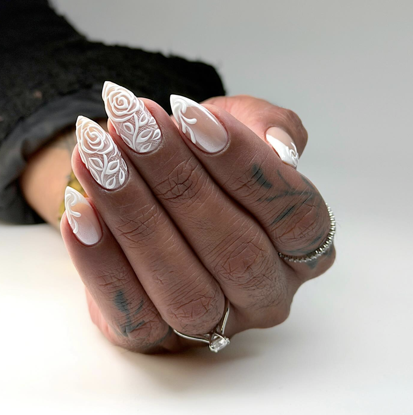 Detailed lace nail art on white almond-shaped nails featuring intricate 3D floral and swirling lace patterns