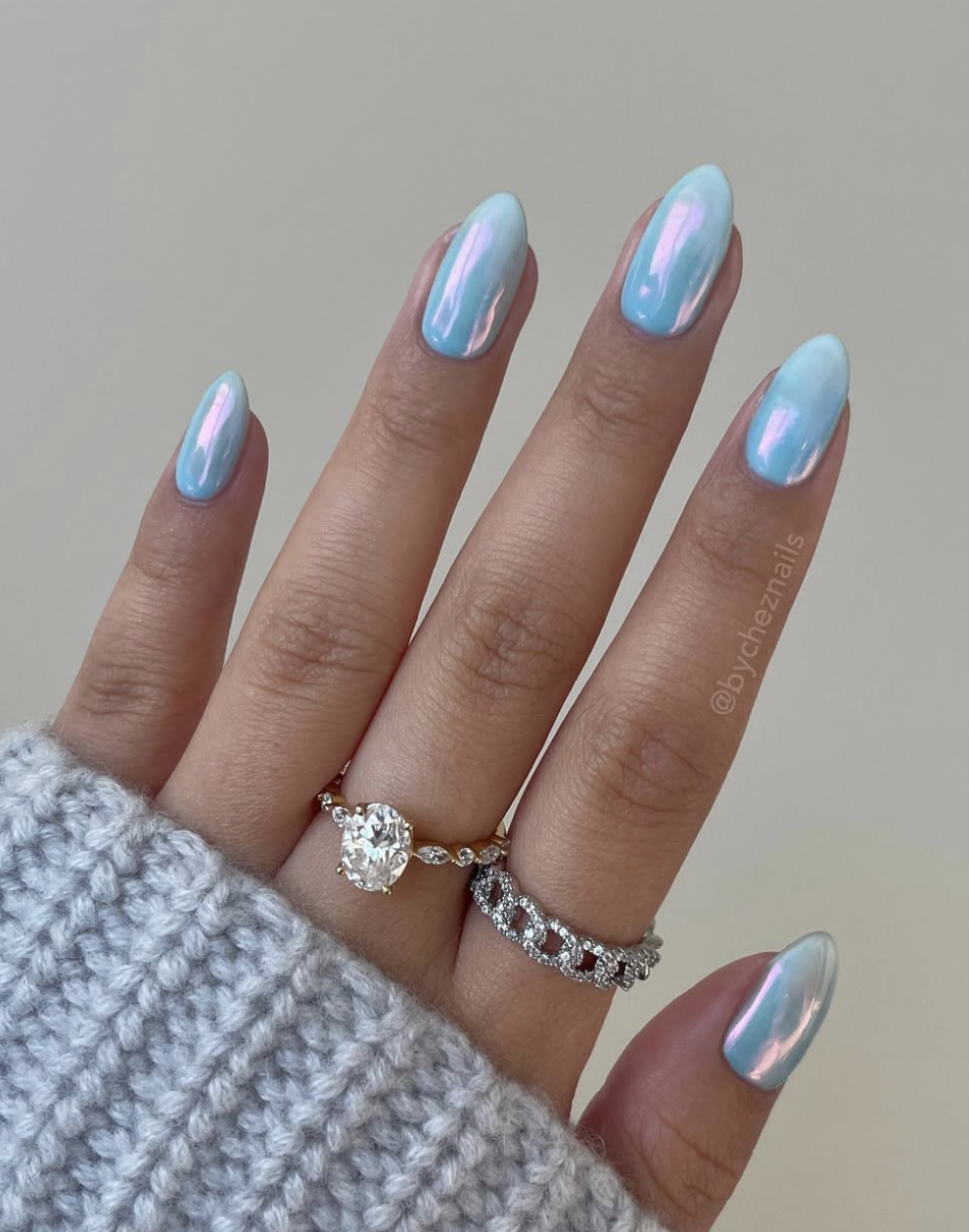 Long almond-shaped gel nails in a soft lavender-blue with a shimmery, holographic chrome finish.