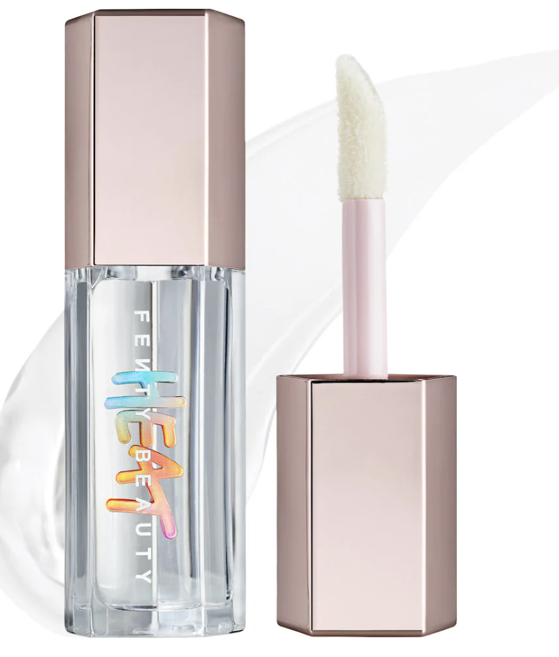: A bottle of Fenty Beauty Gloss Bomb Heat Universal Lip Luminizer + Plumper with a shimmering peach tint and a large doe-foot applicator wand.
