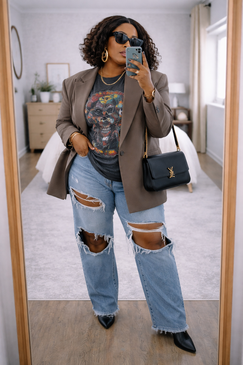 A woman taking a mirror selfie wearing a structured black blazer over a graphic t-shirt and distressed blue jeans, demonstrating how to use layers for structure.