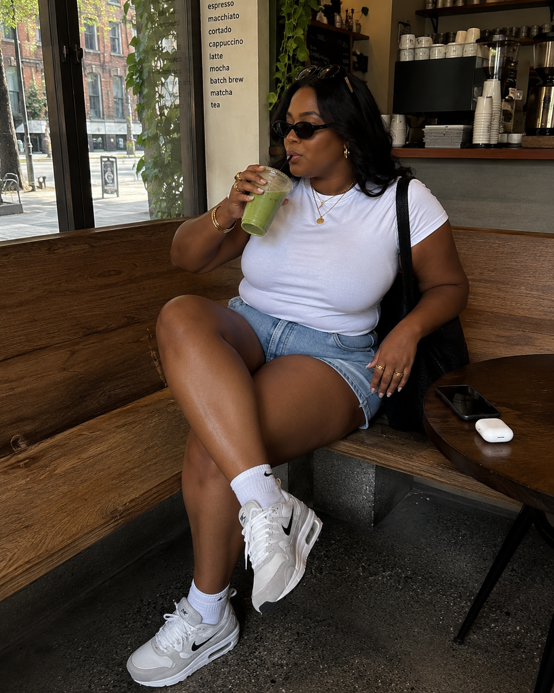 A woman sitting on a bench wearing denim shorts, a white t-shirt, white crew socks, and white athletic sneakers.