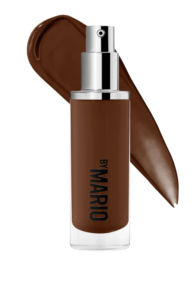 A close-up of the Makeup by Mario SurrealSkin Natural Finish Foundation bottle against a smooth swatch of dark liquid foundation.