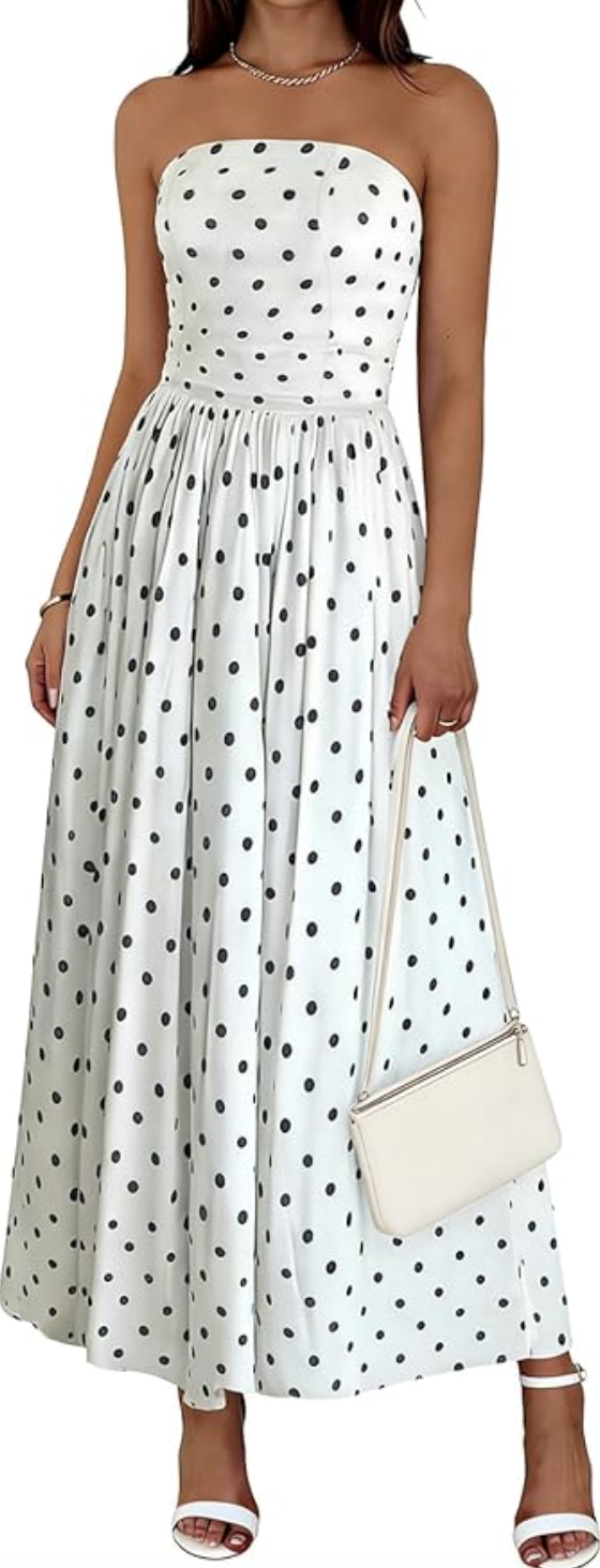 A woman wearing a white strapless maxi dress with black polka dots, featuring a smocked bodice and a flowy tiered skirt on a transparent background.