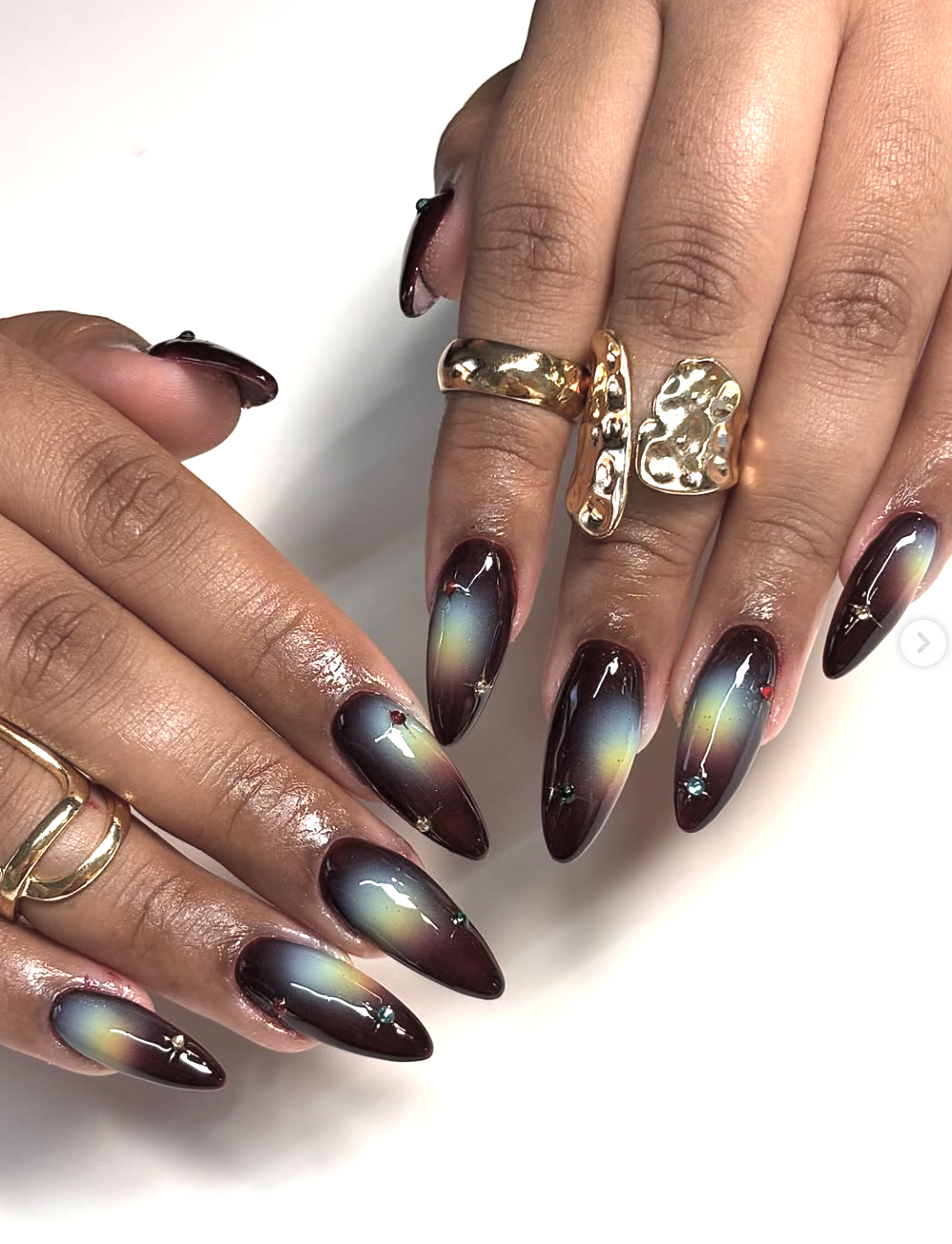 Long almond-shaped nails with a dark base featuring glowing, watercolor-style tie-dye swirls in pastel yellow, green, and blue.